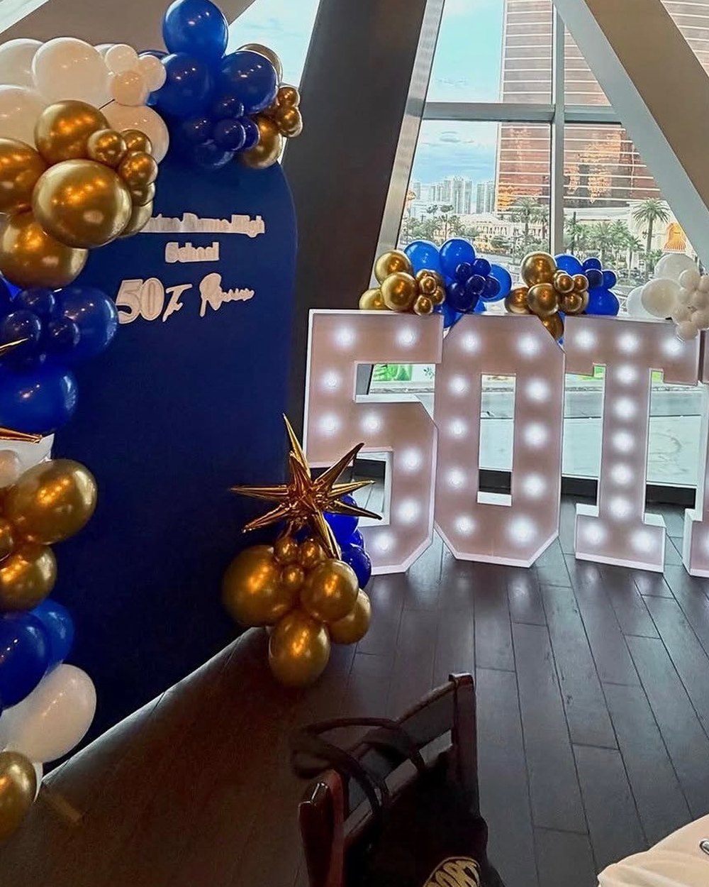 Light-up letters with a navy and gold balloon garland in a room overlooking the Las Vegas Strip