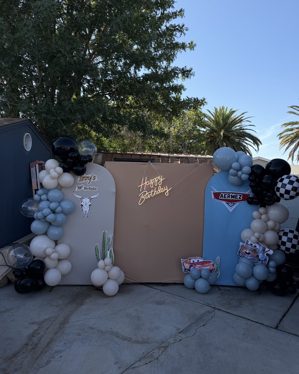 Three panels in cream, tan and blue with printed cutouts, a neon sign and blue, black and cream balloons